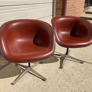 May include: Two brown leather swivel chairs with a silver base. The chairs are in front of a white garage door.