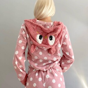 May include: Pink pajamas with white polka dots and an attached pink owl hood. The owl hood has large white eyes.