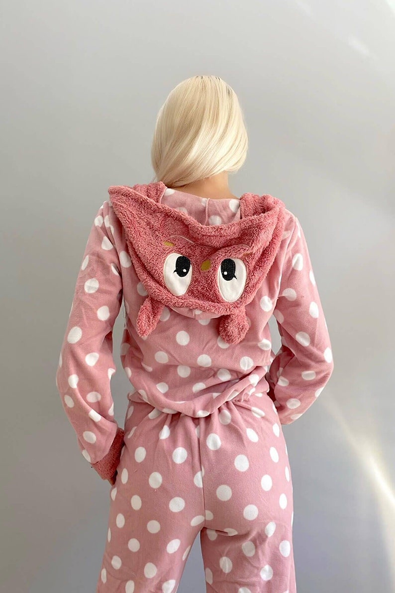 May include: Pink pajamas with white polka dots and an attached pink owl hood. The owl hood has large white eyes.