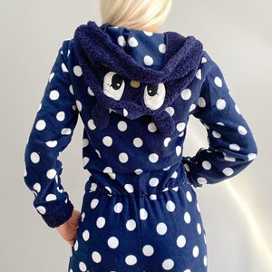 May include: A navy blue hooded jumpsuit with white polka dots. The hood has a plush, black cat face with white eyes.