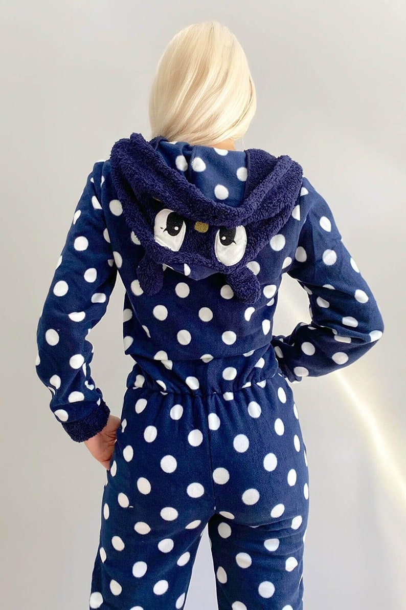 May include: A navy blue hooded jumpsuit with white polka dots. The hood has a plush, black cat face with white eyes.