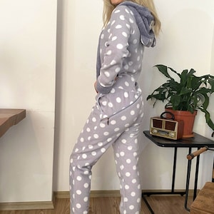 May include: A grey and white polka dot hooded jumpsuit with a zip closure. The jumpsuit has a soft, fuzzy texture.