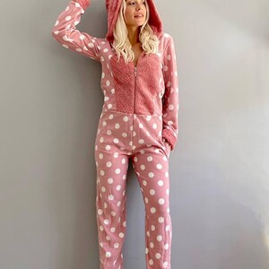 May include: A pink and white polka dot hooded jumpsuit with a fuzzy lining. The jumpsuit has a zipper closure and pockets.