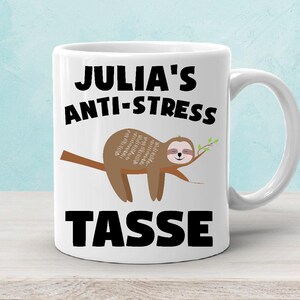 Könnte beinhalten: Weiße Keramiktasse mit einem schwarzen Faultier-Design und dem Text "Julia's Anti-Stress Tasse".