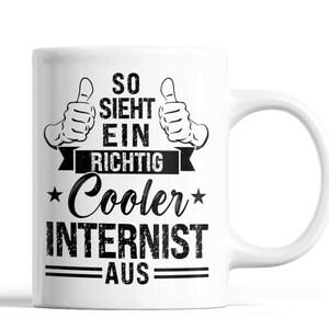 Könnte beinhalten: Weiße Keramiktasse mit schwarzer Grafik. Die Grafik enthält zwei Daumen hoch, die Worte "SO SIEHT EIN RICHTIG Cooler INTERNIST AUS" in einer kräftigen, stilisierten Schriftart und Sternakzente. Die Tasse hat einen gebogenen Griff.