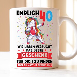 Könnte beinhalten: Weiße Keramiktasse mit einem bunten Einhorn, das dabbt, und dem Text "ENDLICH 40" in Blau und Rot. Der Text "WIR HABEN VERSUCHT DAS BESTE GESCHENK FÜR DICH ZU FINDEN ABER DU HAST JA BEREITS UNS" ist unter dem Einhorn gedruckt.