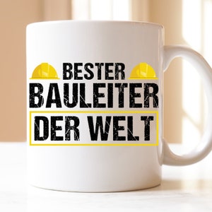 Könnte beinhalten: Weiße Keramiktasse mit einem schwarzen und gelben Design. Die Tasse zeigt den Text "BESTER BAULEITER DER WELT" mit zwei gelben Bauhelmen auf beiden Seiten des Textes.