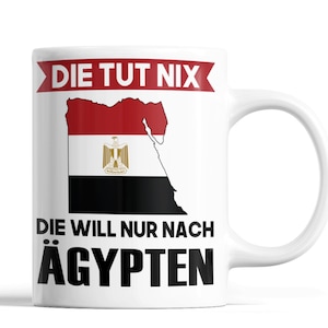 Könnte beinhalten: Weiße Keramik-Tasse mit dem ägyptischen Flaggen-Design und den deutschen Sätzen „DIE TUT NIX“ und „DIE WILL NUR NACH ÄGYPTEN“. Die Tasse hat einen gebogenen Griff und eine glänzende Oberfläche.