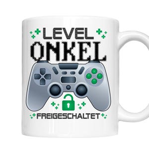 Könnte beinhalten: Weiße Keramiktasse mit einem grünen und grauen Videospiel-Controller-Motiv. Der Text "LEVEL ONKEL FREIGESCHALTET" ist auf die Tasse gedruckt.
