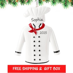 May include: A white chef's coat ornament with a chef's hat, a red neckerchief, and black buttons. The name "Sophia" and the year "2025" are printed on the ornament. The ornament is designed for the holiday season.