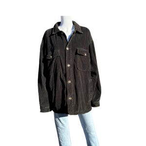 May include: A black corduroy button-up shirt with long sleeves and two flap pockets. The shirt is on a mannequin and has a relaxed fit.