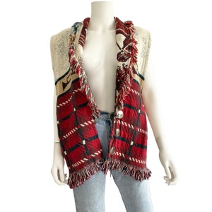 May include: A sleeveless vest with a red, white, and blue plaid pattern and fringe trim. The vest has a button closure and a woven design.