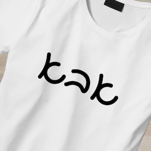 May include: White t-shirt with the Hebrew word "kak" printed in black. The shirt is made of a soft material and has a classic crew neck design. The text is centered on the front of the shirt.