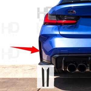 May include: A close-up of a blue car's rear bumper with black trim and two black vertical stripes on the side. The car has a black rear diffuser with two exhaust pipes.