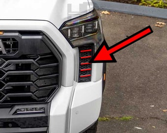 May include: White pickup truck with a black grille and red accents on the front bumper. The red accents are highlighted with a red arrow.
