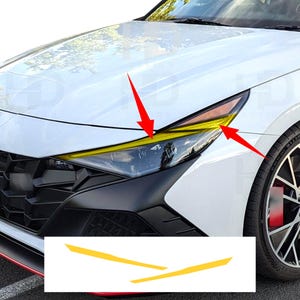 May include: A white car front end featuring a yellow adhesive vinyl overlay applied to the upper section of the headlight assembly. Two red arrows point to the yellow trim piece, and a separate graphic shows the two yellow strips in isolation.
