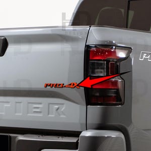 May include: Close-up of a gray truck's rear with a black taillight and the orange text "PRO-4X" with a red arrow pointing towards the taillight. The word "TIER" is visible below the taillight.