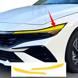 May include: A white car front end featuring a yellow vinyl overlay applied to the upper portion of the headlight assembly. A red arrow points to the yellow tint on the headlight. Two additional yellow vinyl strips are shown below the car.