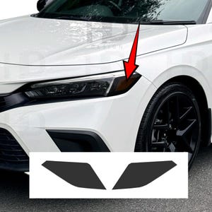 May include: A white car with black wheels and a black headlight assembly. Two black headlight covers are displayed below the car. The car's headlight has an amber-colored side marker.