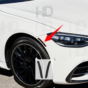 May include: A white car with black rims and a black tire. The car has a black trim around the wheel well and a brown accent piece. The image also shows a sticker with the letters "V". The car has the text "HD DESIGN".