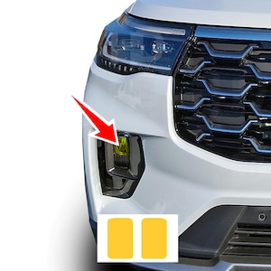 May include: A white vehicle front bumper section featuring a glossy black grille with blue accents and a clear headlight. A red arrow points to a yellow fog light cover, with two additional yellow rectangular adhesive covers shown below.