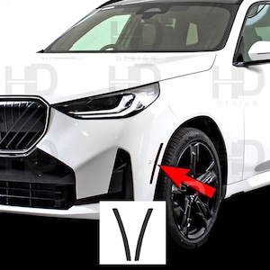 May include: A white car with black accents, including a black front grill and black rims. The image highlights a pair of black vertical trim pieces, shaped like a "V", with a red arrow pointing towards them. The text "HD DESIGN" is visible.