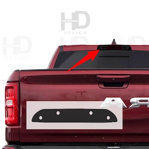 May include: A red pickup truck with a black tailgate. The tailgate has a black trim piece with four holes in it. The truck has a black rear window and a black rear bumper.