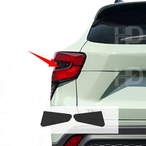 May include: A white car with black rear bumper guards. The car has a red taillight and a black rear window.