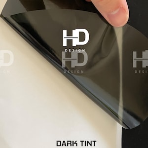 May include: A black vinyl sheet with the text "HD DESIGN" printed on it. The sheet is being peeled back to reveal a white surface with the text "DARK TINT" printed on it.