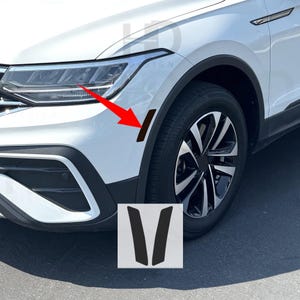 May include: Black car side marker light vinyl overlays. The image shows a white car with a black overlay applied to the side marker light. The overlays are in a V shape. The car has black tires and rims.