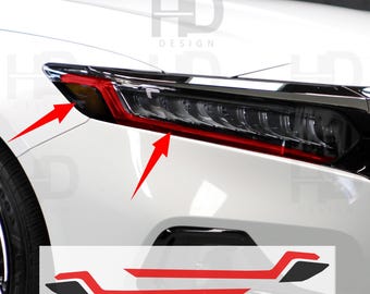 May include: Close-up of a white car's headlight assembly with a black and red accent design. The image includes a sticker with a red and black design. The text "HD DESIGN" is visible in the background.