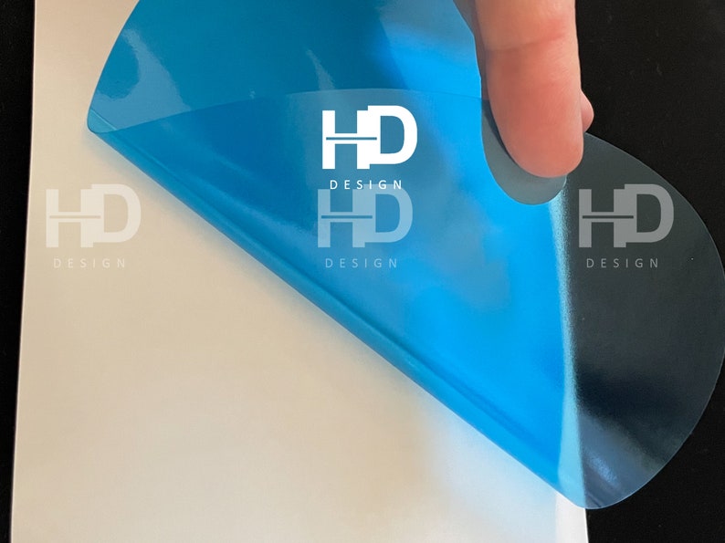 May include: A blue transparent sticker with the text "HD DESIGN" printed in white. The sticker is being peeled off of a white surface.