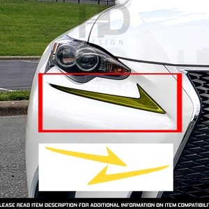 May include: A white car with a yellow accent on the front headlight. The accent is shaped like a sharp arrow. The car has a black grille with a diamond pattern.