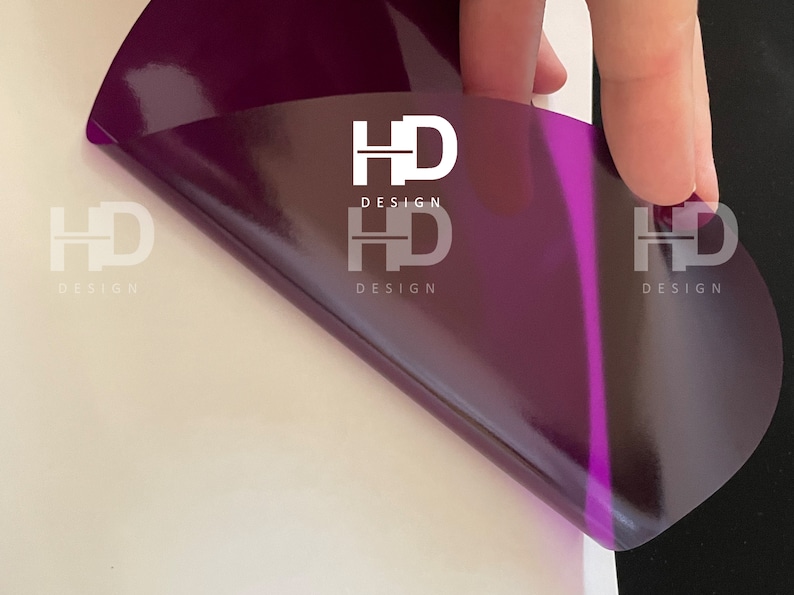 May include: A close-up of a purple vinyl sticker with the text "HD DESIGN" printed on it. The sticker is being peeled off of a white surface.
