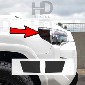 May include: A white car with black headlight covers. The car has a black tire and a black bumper. The image shows two black headlight covers that are sold separately.