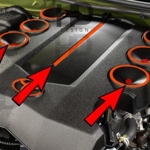 May include: Close-up of a black engine cover with orange accents. The cover has six circular openings with orange trim. The word "DESIGN" is visible on the cover.