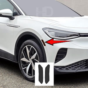 May include: White car with black accents, a black wheel, and a set of two black car accessories. The accessories are on a white background. A red arrow points to a brown area on the car.