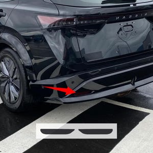 May include: Black car bumper with a red reflector and a parking sensor. The image also shows a pair of black bumper protectors.