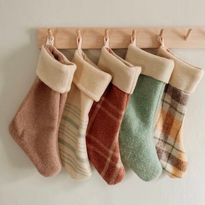 Peut inclure: Quatre chaussettes de Noël décoratives avec différents motifs à carreaux en marron, vert et beige. Les chaussettes sont accrochées à un support en bois.