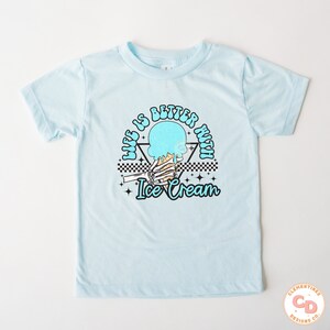 May include: Light blue t-shirt with a graphic of a skeleton hand holding a melting ice cream cone. The text "Life is better with ice cream" is written in a retro font around the graphic.