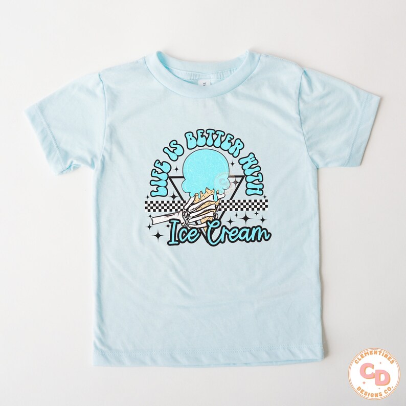 May include: Light blue t-shirt with a graphic of a skeleton hand holding a melting ice cream cone. The text "Life is better with ice cream" is written in a retro font around the graphic.