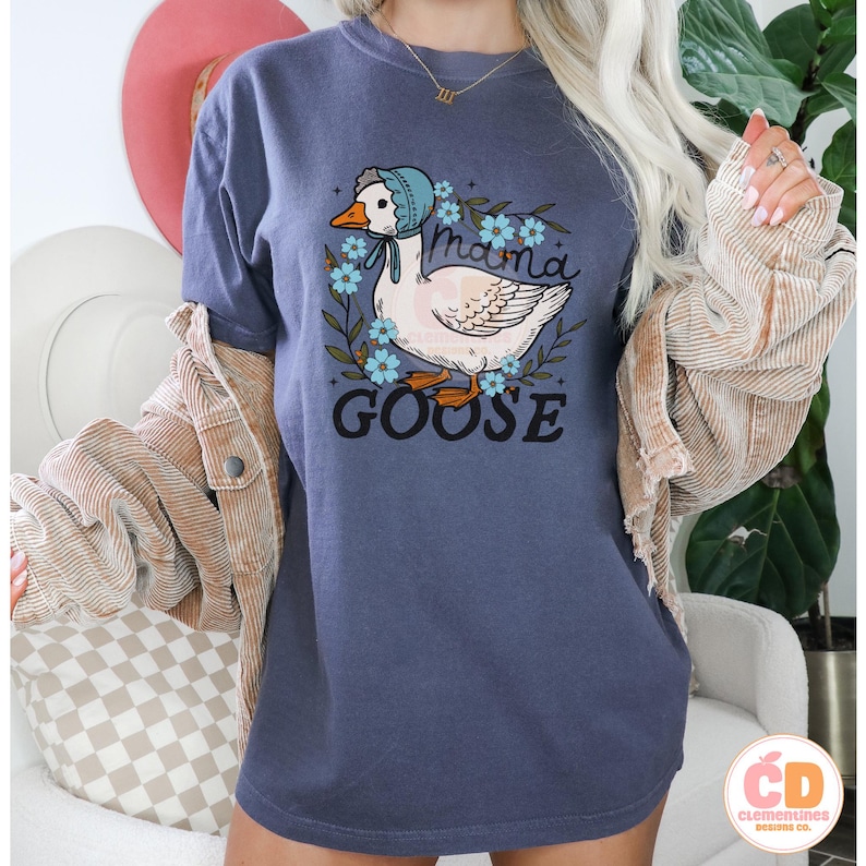 May include: A blue t-shirt with a white goose wearing a blue bonnet and surrounded by blue flowers. The text "Mama Goose" is printed on the shirt.