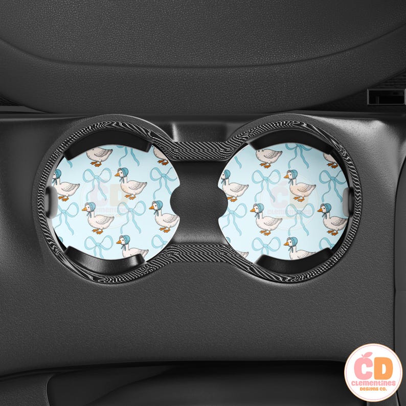 May include: Two black car cup holders with blue and white patterned inserts featuring a repeating design of white ducks wearing blue bonnets and blue bows.