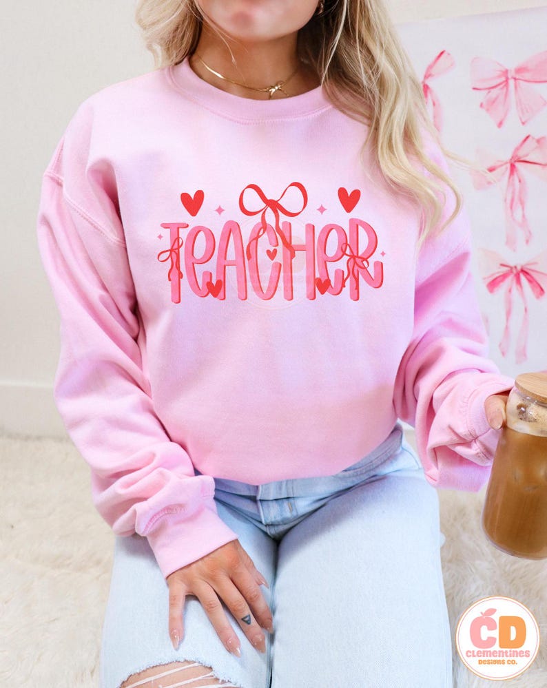 May include: Pink sweatshirt with the word "TEACHER" in red and white lettering with hearts and bows.