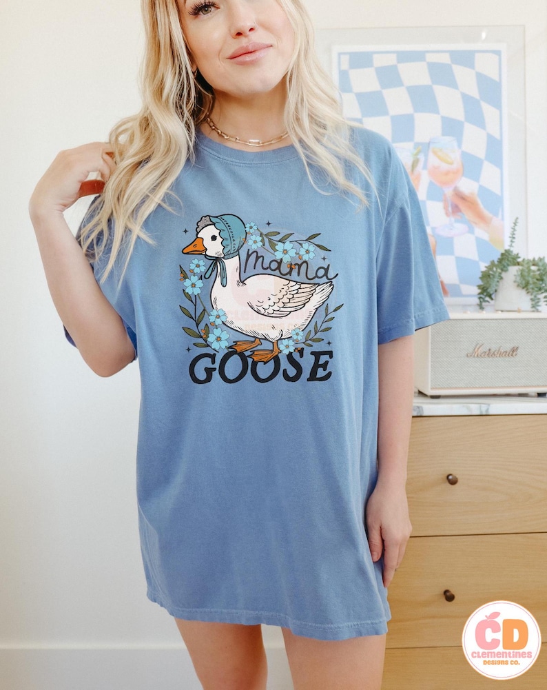 May include: A light blue t-shirt with a graphic of a white goose wearing a bonnet and surrounded by blue flowers. The text "mama goose" is printed below the goose.