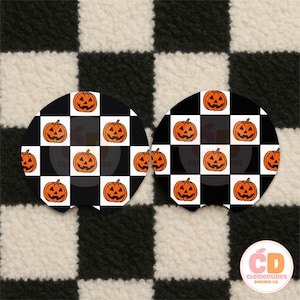 May include: Two round car coasters with a black and white checkered pattern. Each coaster features a grid of orange jack-o'-lanterns. The background is a black and white checkered pattern.