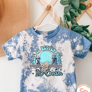 May include: A blue tie-dye t-shirt with a graphic of a skeleton hand holding a melting ice cream cone. The graphic has the text "Life is better with Ice Cream" in a retro font.