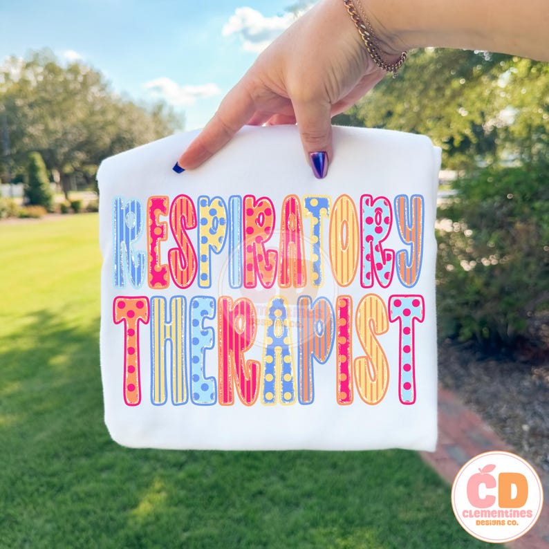 May include: White t-shirt with the words "RESPIRATORY THERAPIST" in colorful, patterned letters. The letters are in shades of blue, orange, yellow, and pink. The shirt is held up by a hand with blue nail polish.