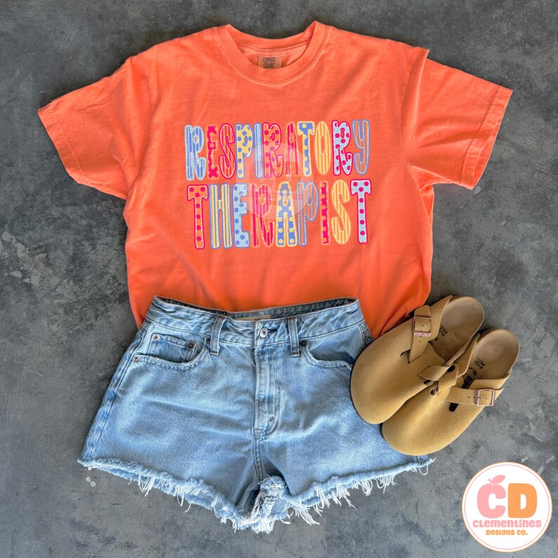 May include: An orange t-shirt with the words "RESPIRATORY THERAPIST" in colorful letters. The shirt is paired with light blue denim shorts and tan sandals. The image is a flat lay, showcasing casual apparel.