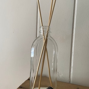 May include: A clear glass bottle with a black lid and wooden sticks inside. The bottle has a textured surface and is sitting on a wooden surface.